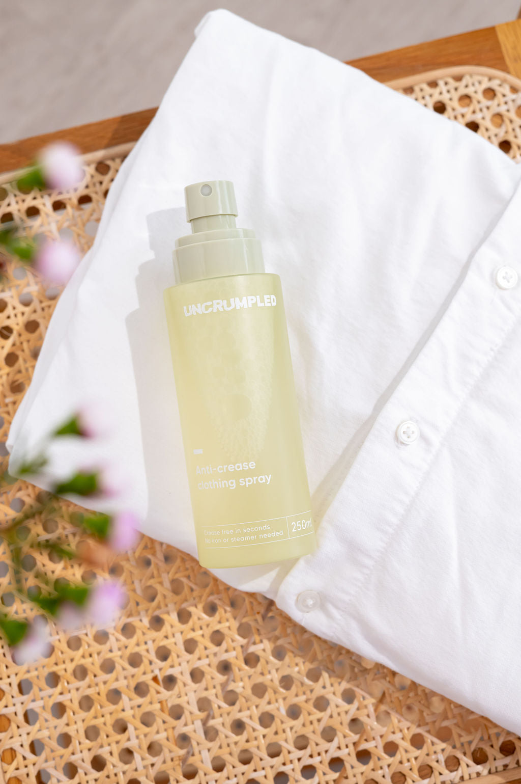 Uncrumpled regular-sized anti-crease spray bottle with its cap off, placed on top of a folded white shirt and furniture.