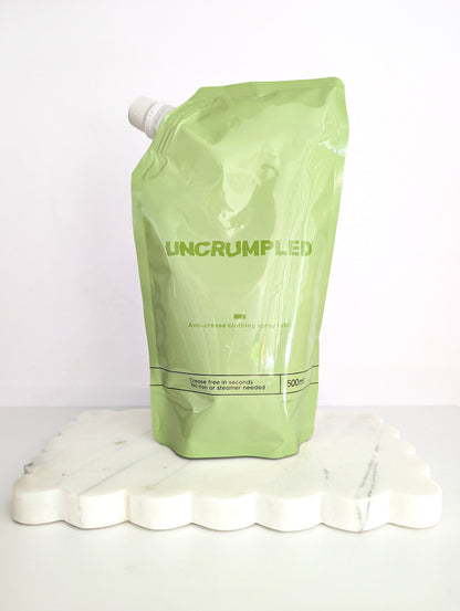 Green Uncrumpled refill pouch standing on a white platform against a white background.